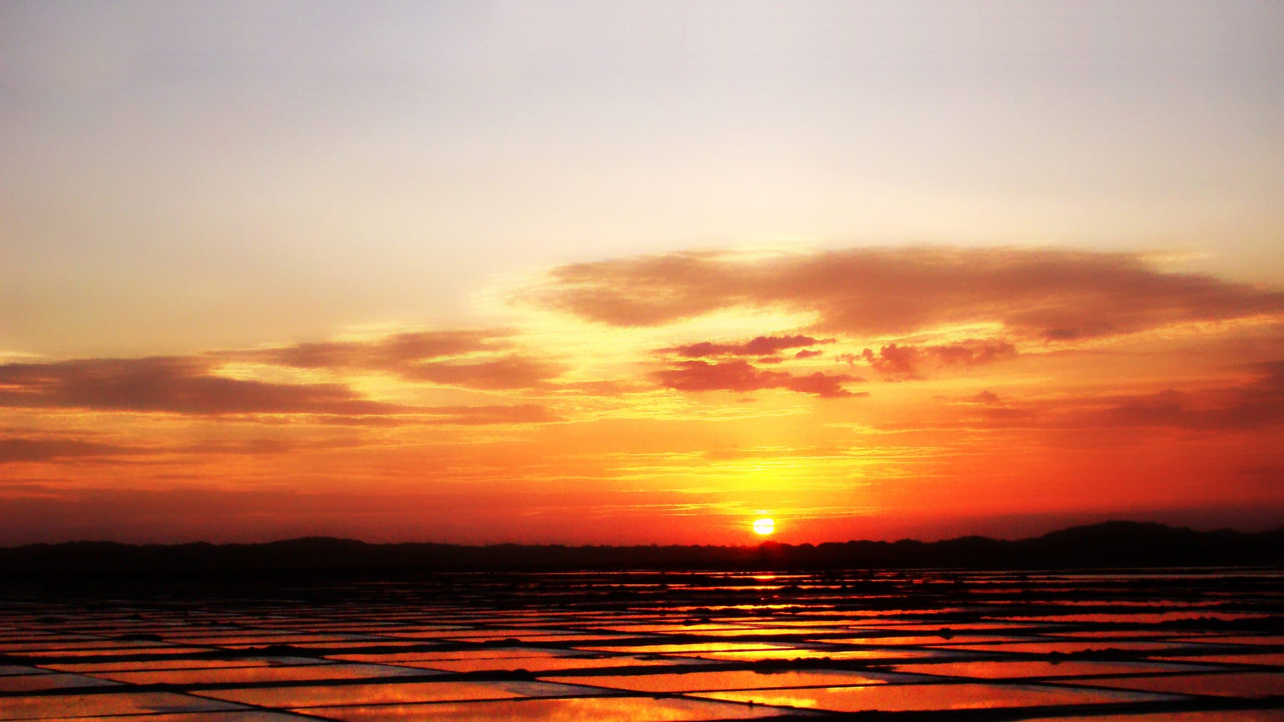 Pôr do sol alaranjado sobre as salinas de Cabo Frio, com o sol refletido nos tanques de evaporação